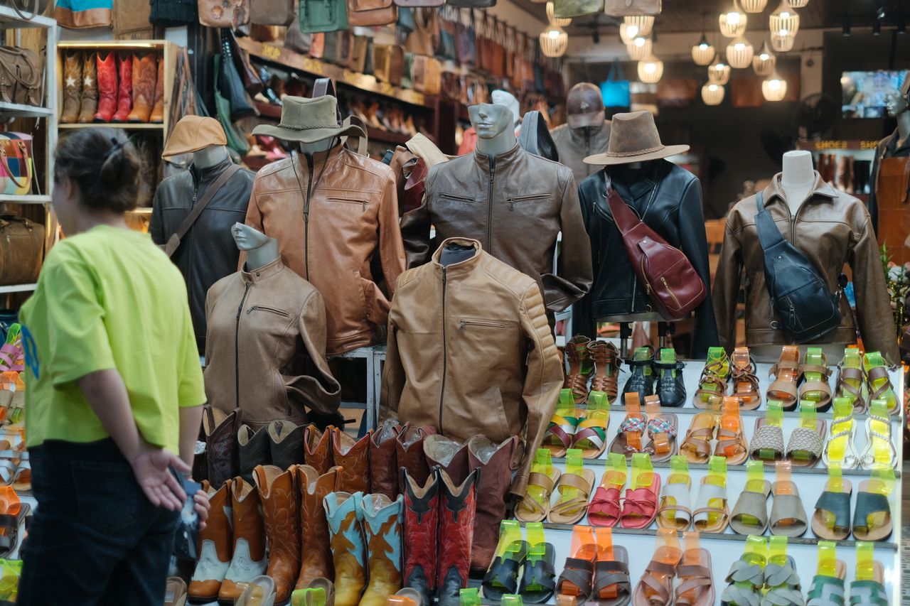 about-02 Mannequins displaying diverse leather goods at a bustling market stand.