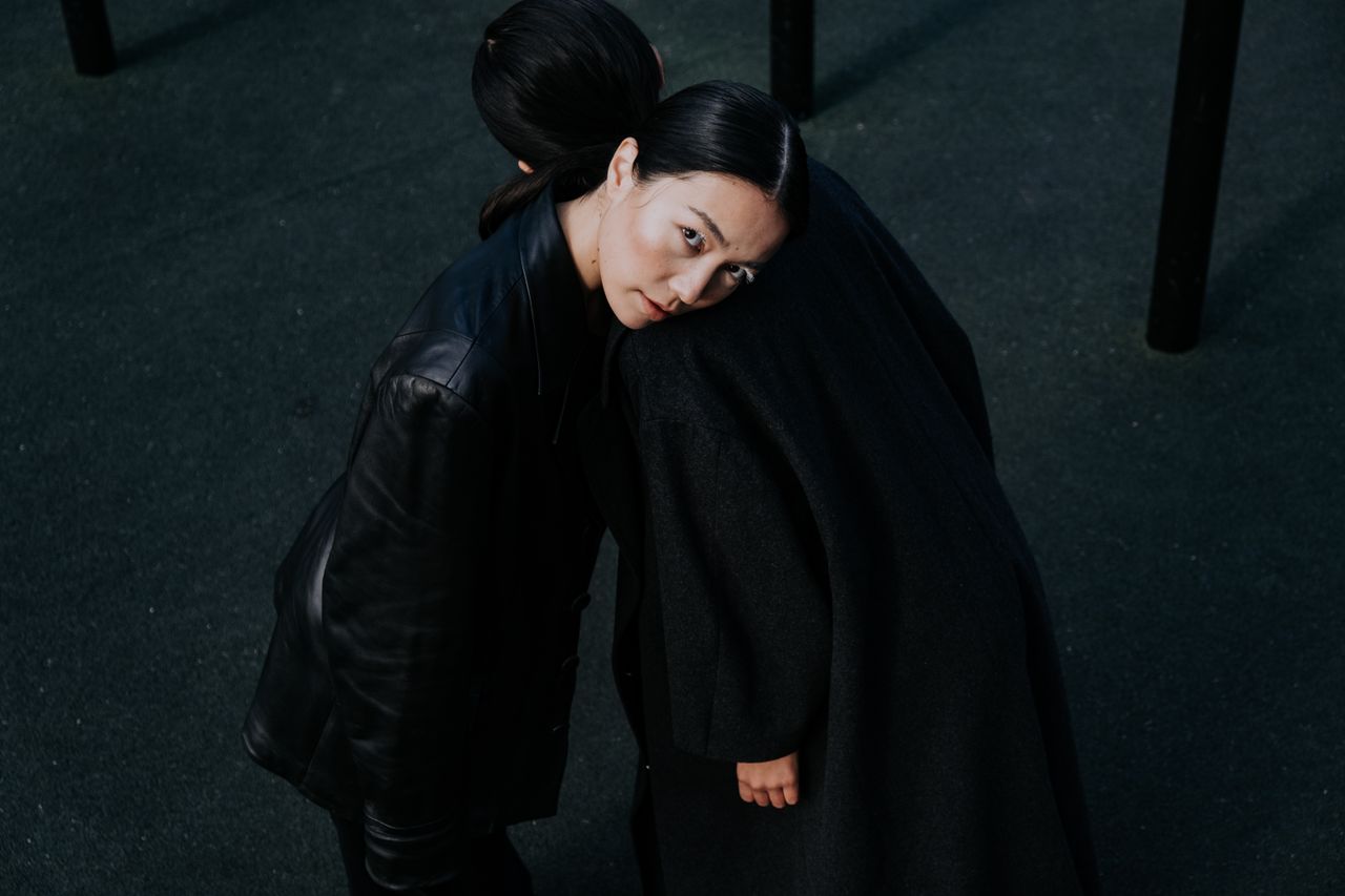 our-experience Stylish and dramatic portrait of two women embracing in dark coats outdoors, showcasing avant-garde fashion.