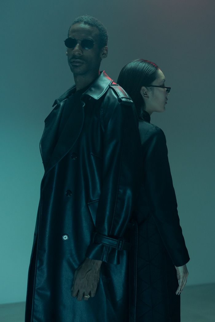 Two individuals stand back to back in cyberpunk-inspired black leather coats, embodying futuristic fashion.