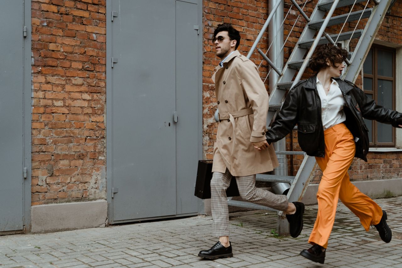 Young stylish couple holding hands and running on an urban street, showing affection and joy.